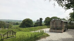 Un chemin de gravier mène à un banc en bois et à une structure abritée agrémentée d’un jardin.