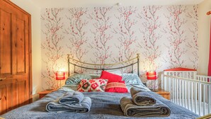 Ein Schlafzimmer mit einem Holzschrank, einem Bett mit Metallgestell, zwei Nachttischlampen und einem Babybett mit roter Matratze.