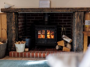 Una chimenea con estufa de leña, un cubo blanco y una cesta de leña.