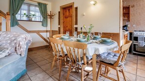 A dining area with a wooden table set for four, surrounded by wooden chairs. A staircase with a wooden railing is visible to the left. - Purbeck View - UK36320 (Holly Hedge Farm)