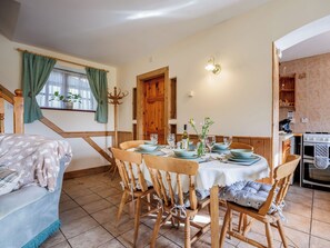 Un comedor con una mesa de madera dispuesta para cuatro personas, rodeada de sillas de madera. Se observa una escalera con barandilla de madera a la izquierda.