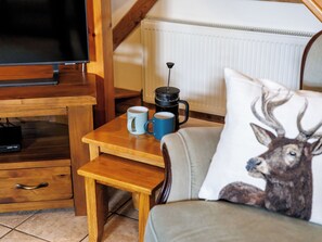 A cozy room with a wooden TV stand, a small table with two mugs, a coffee maker, and a sofa with a deer pillow.