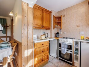 A compact kitchen with wooden cabinets, a gas stove, a small refrigerator, and a dining area with a table and chairs.