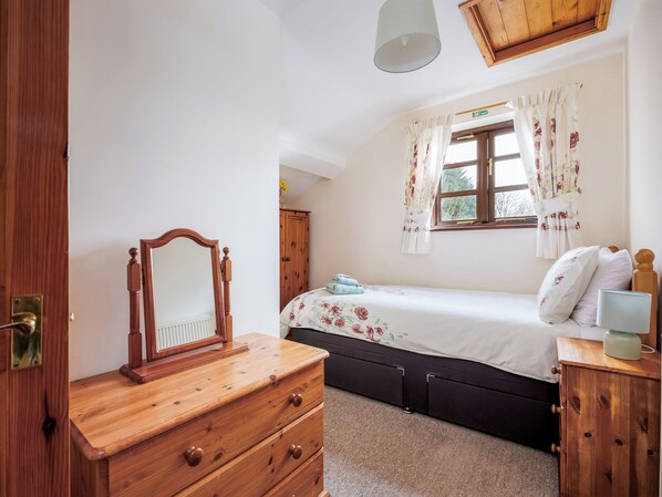 Un dormitorio con cómoda de madera, cama con ropa de cama floral, ventana con cortinas florales y armario de madera.