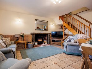 A cozy living room with a fireplace, a television, and a staircase.