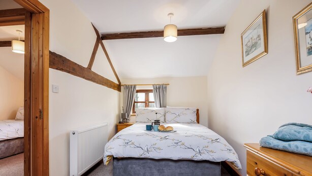 A bedroom with a bed, a dresser, a radiator, a wooden ceiling, and a window with curtains. - Purbeck View - UK36320 (Holly Hedge Farm)