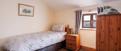 Un dormitorio con cama, mesita de noche, armario de madera, ventana con cortinas y un cuadro enmarcado en la pared.