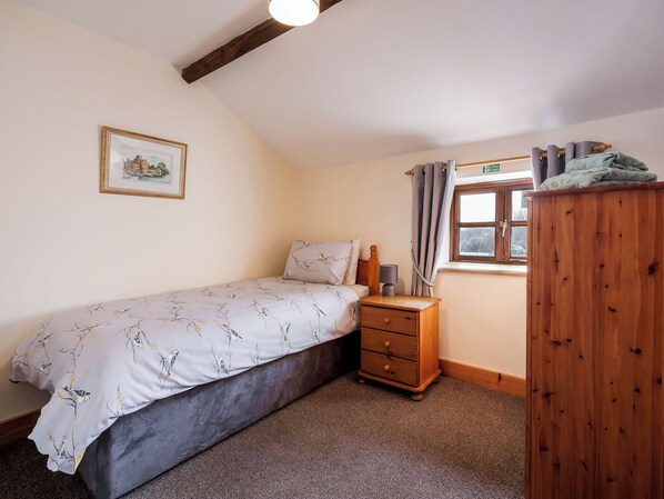 A bedroom with a bed, a nightstand, a wooden wardrobe, a window with curtains, and a framed picture on the wall.