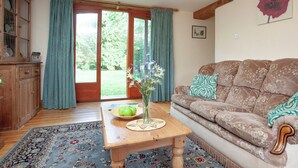 A cozy living room with a wooden coffee table, a brown sofa with patterned cushions, a floral rug, and a view of a garden through a glass door. - Coachman's lodge - UK35952 (Kingsbridge)
