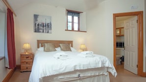 A neatly made bed with white linens, two bedside tables with lamps, a painting of people with umbrellas, and a wooden door leading to a bathroom. - Coachman's lodge - UK35952 (Kingsbridge)