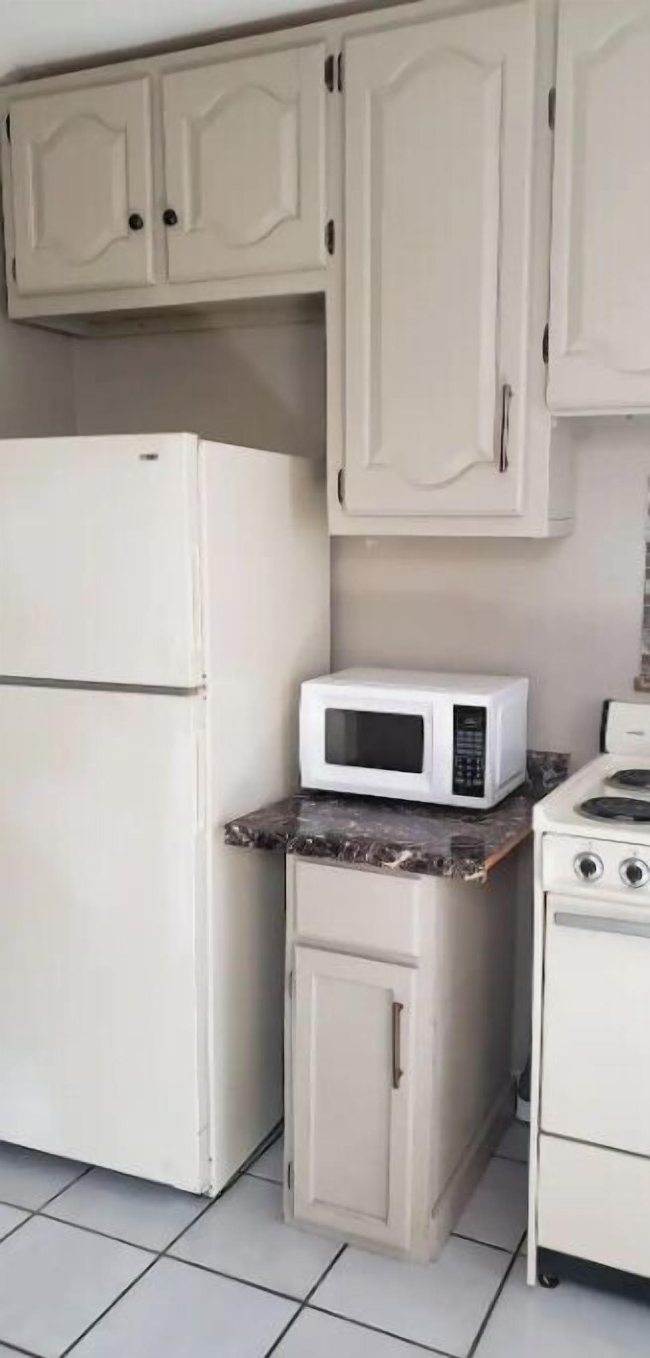 Une cuisine avec des armoires blanches, un réfrigérateur blanc, un four à micro-ondes et une cuisinière.