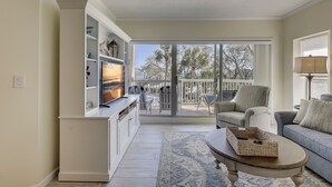 A spacious living room with a large TV, a sofa, a coffee table, and a view of the outdoors through a sliding glass door. - 206 Barrington Arms- OCEANFRONT and BEAUTIFUL (Hilton Head Island)