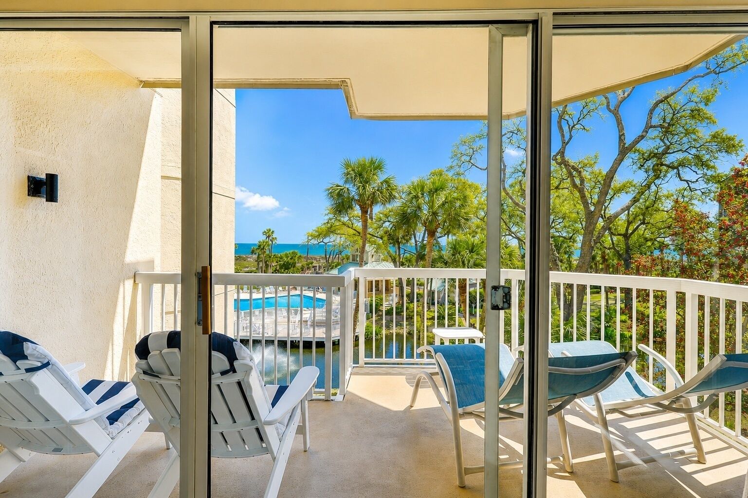 A balcony with white chairs and a table, overlooking a pool and a view of the ocean.