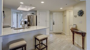 A modern kitchen with a central island, white cabinetry, and a stainless steel refrigerator. - 206 Barrington Arms- OCEANFRONT and BEAUTIFUL (Hilton Head Island)