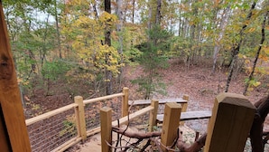 Una terraza de madera con barandilla rústica, rodeada por un bosque con follaje otoñal.