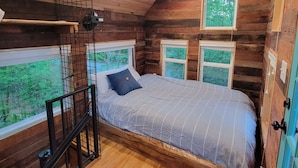 Un dormitorio acogedor tipo cabaña de madera, con cama, ventana y una mesita.