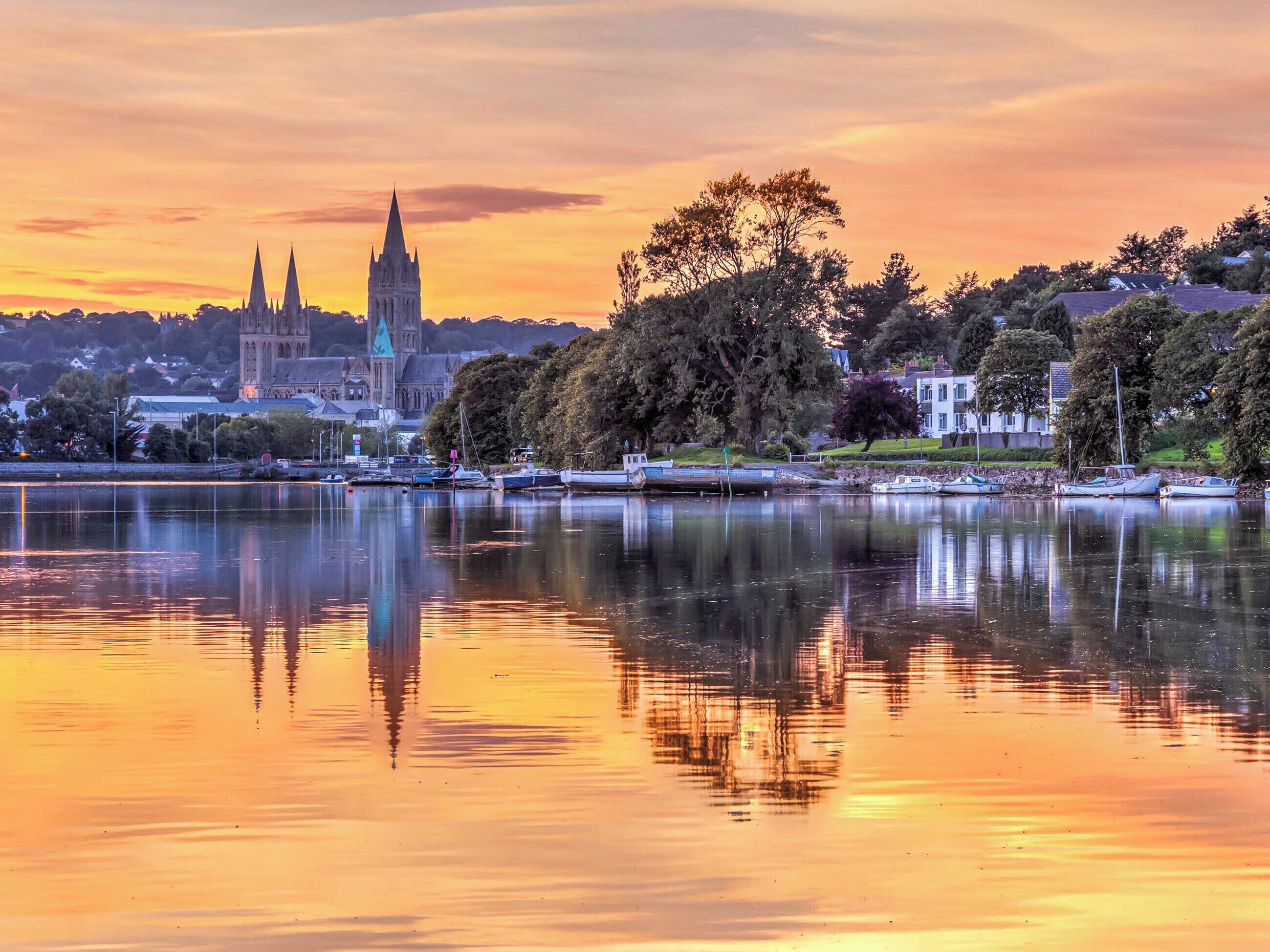 Un lago tranquilo con barcos, una iglesia histórica y edificios residenciales al atardecer.