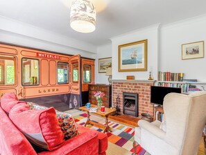 A living room with a vintage train-themed wall, a fireplace, and a bookshelf. - A charming bungalow with an LSWR train attached. (Dorchester)