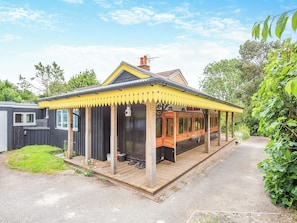 A house with a covered porch and a train carriage attached to the back. - A charming bungalow with an LSWR train attached. (Dorchester)