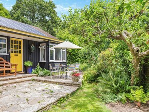 Une maison jaune avec un patio en pierre, un banc en bois et une table avec des chaises.