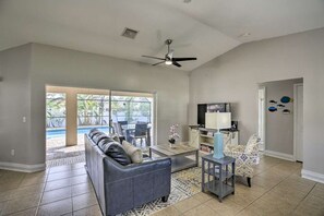 A spacious living room with a grey sofa, a coffee table, and a TV. There is a sliding glass door leading to a pool area. - Private Home w/ fence/SPA/Pool & Screened Lanai! (Cape Coral)