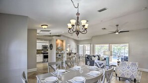 A spacious dining area with a chandelier, a kitchen in the background, and a living area with a sofa and patterned chair. - Private Home w/ fence/SPA/Pool & Screened Lanai! (Cape Coral)