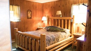 A wooden-paneled room with a bed, two bedside tables, and a lamp.