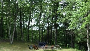 A wooden deck with a bench and a metal chair, overlooking a grassy area with picnic tables and chairs.