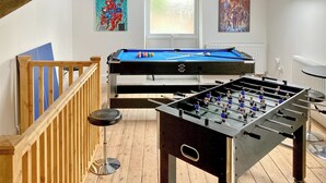 A room with a pool table, foosball table, wooden railing, and two posters on the wall.
