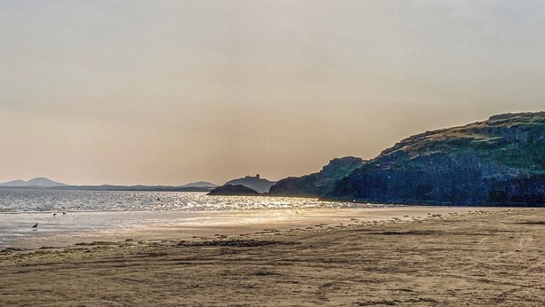 A beach with a clear sky, calm sea, and distant hills.