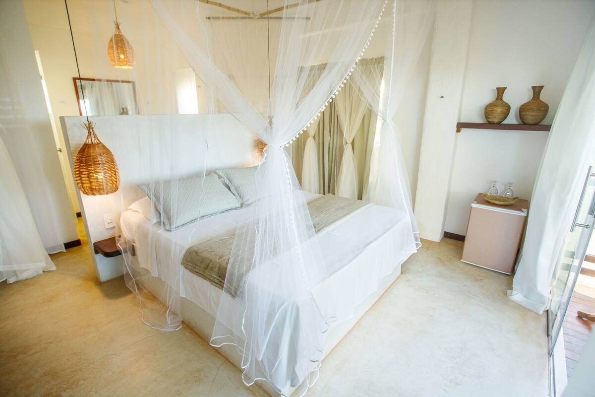 A bedroom with a canopy bed, bedside tables, a mirror, and a shelf with vases.