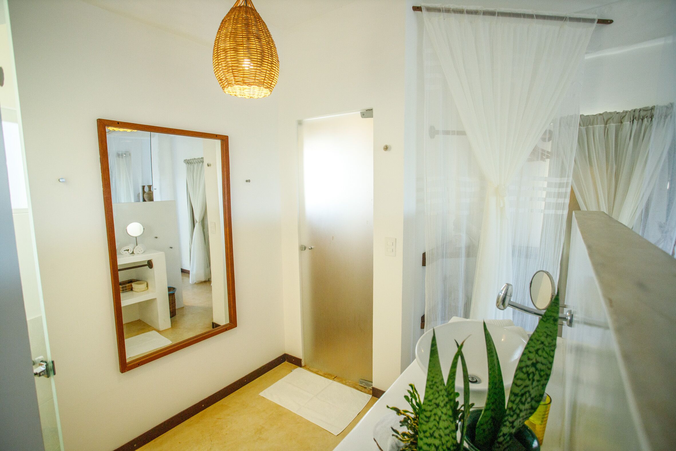 A bathroom with a large mirror, a sink, a shower, and a hanging light fixture.