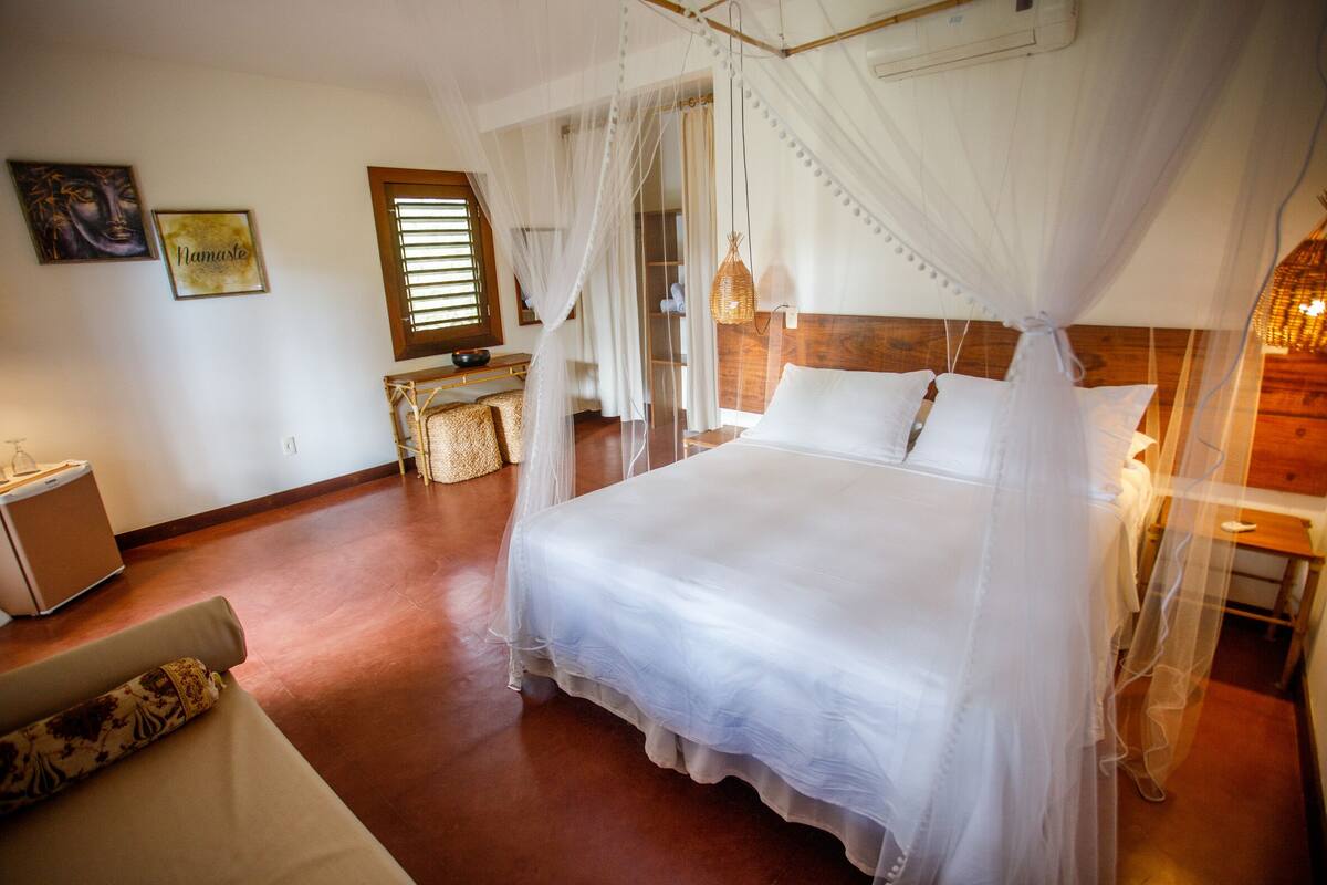 A bedroom with a four-poster bed, a bedside table, a chair, and a small desk.