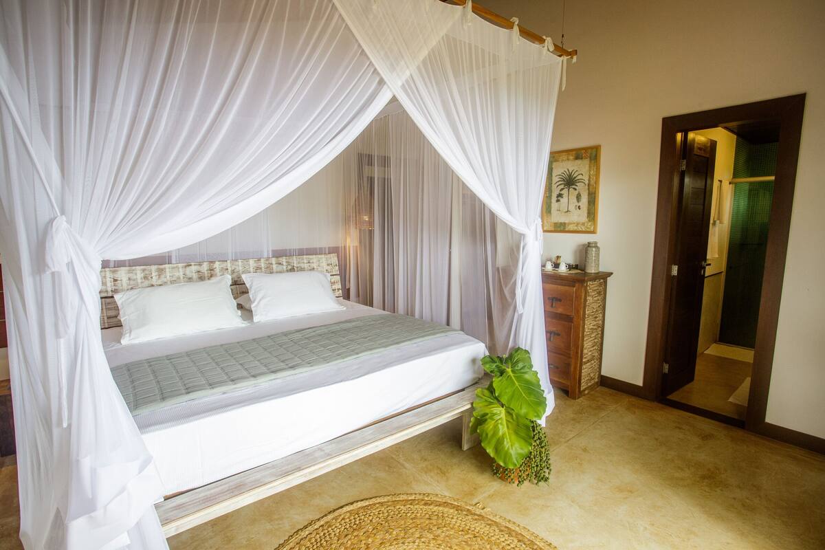 A bed with a canopy, a bedside plant, and a wooden cabinet with a mirror.