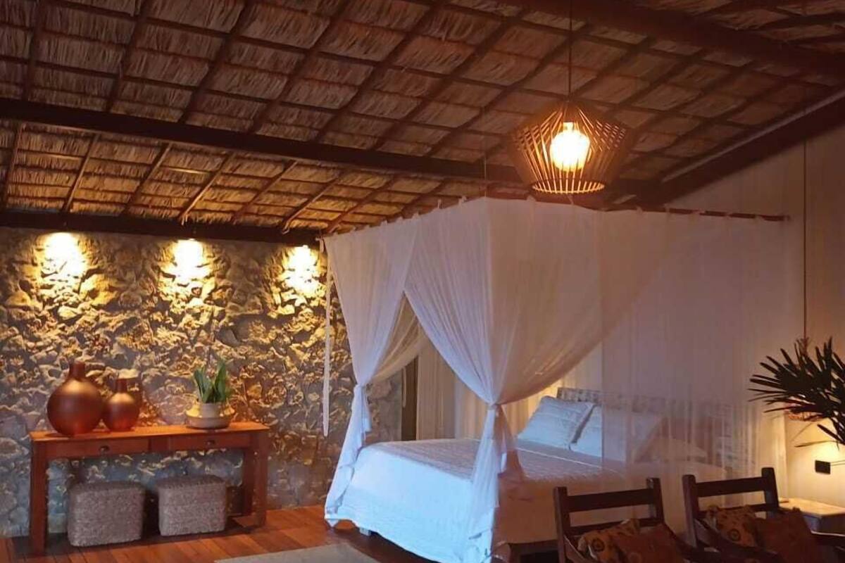 A room with a bed under a canopy, a stone wall, a wooden floor, and a hanging light fixture.