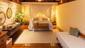A bedroom with a canopy bed, wooden flooring, a stone wall, and a small bedside table with a plant. - Hara Pousada e SPA (São Miguel do Gostoso)