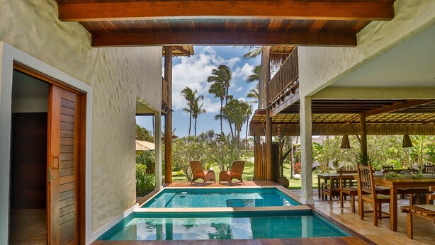 A pool area with two lounge chairs, a dining table with chairs, and a covered seating area. - Hara Pousada e SPA (São Miguel do Gostoso)