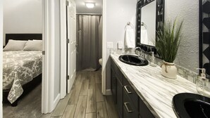 A modern bathroom with a large mirror, a sink, and a shower. - Bright and Gorgeous! Fish across the street - Lake Access in Branson! (Branson)