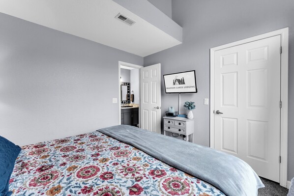 A bedroom with a bed, a dresser, a TV on the wall, and a door to another room.