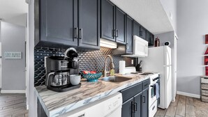 A modern kitchen with dark cabinets, a marble countertop, a coffee maker, and a dishwasher. - Bright and Gorgeous! Fish across the street - Lake Access in Branson! (Branson)