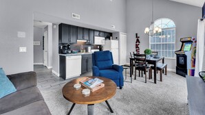 A modern living room with a blue armchair, a coffee table, and a dining area with a table and chairs. - Bright and Gorgeous! Fish across the street - Lake Access in Branson! (Branson)