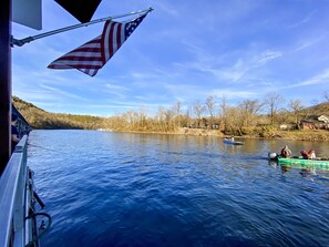 A river scene with a boat, an American flag, and a house in the background. - Bright and Gorgeous! Fish across the street - Lake Access in Branson! (Branson)
