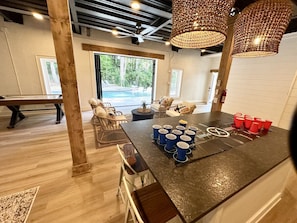 A room with a pool view, wicker furniture, and a table with cups. - Living the Dream: Luxurious Lakeside Home with New Private Pool and Poolhouse (Mooresville)