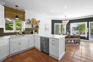 A modern kitchen with white cabinets, a dishwasher, a wooden ceiling, and a dining area with a table and chairs.