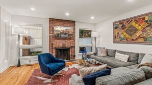 Ein Wohnzimmer mit einem Kamin aus Ziegelsteinen, einem blauen Sessel, einem grauen Sofa und einem bunten Wandteppich.