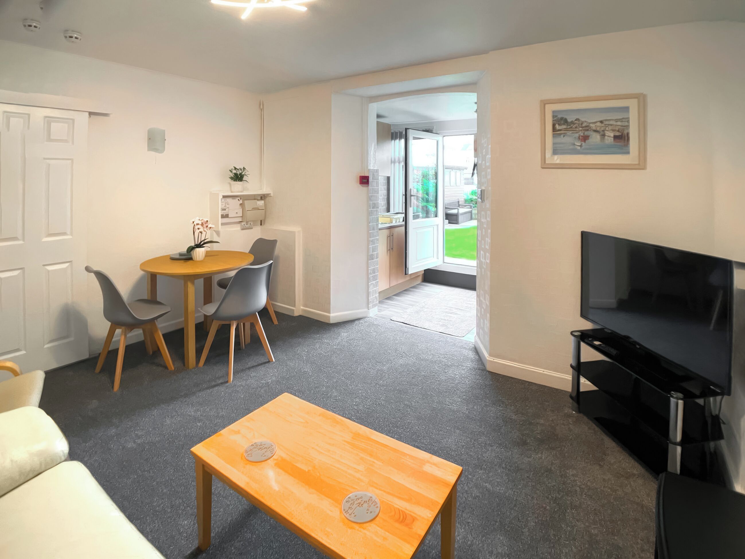A living room with a TV, a dining area with a table and chairs, and a door leading to a balcony.
