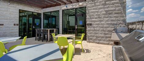 An outdoor patio with tables and chairs, a grill, and a stone wall.