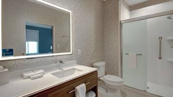 A modern bathroom with a large mirror, dual sinks, a toilet, and a glass shower enclosure.