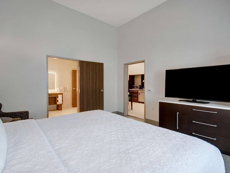 A hotel room with a large bed, a flat-screen TV, a wardrobe, and a bathroom visible through an open door.