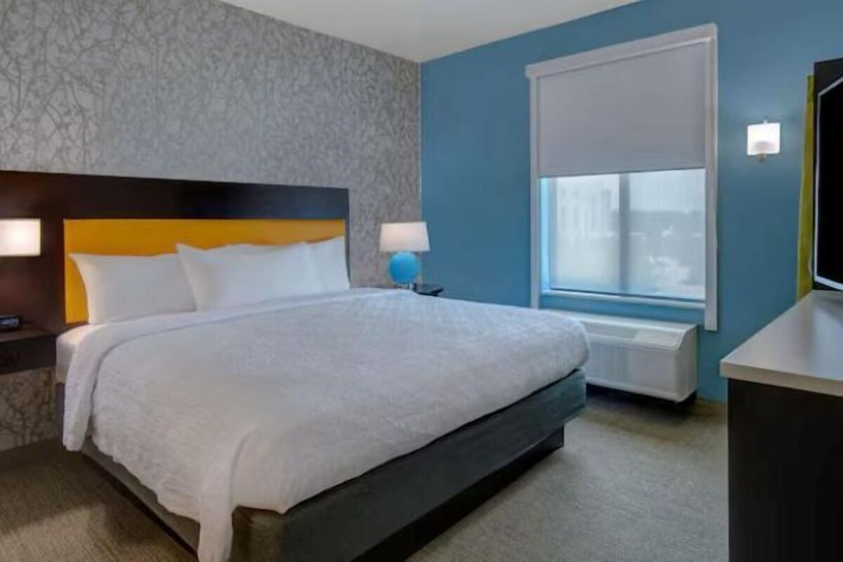 Habitación de hotel con cama, lámparas de noche, ventana con vistas y escritorio con lámpara.